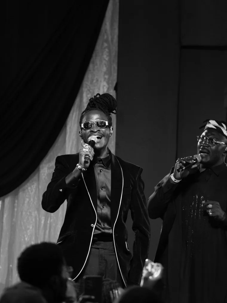 Two Kodong Klan vocalists singing side by side, black and white.